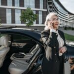 Senior businesswoman making a phone call beside a luxury vehicle in an urban setting.