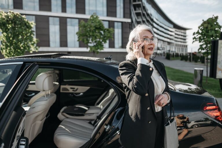 Senior businesswoman making a phone call beside a luxury vehicle in an urban setting.