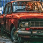 An atmospheric image of a rust-covered vintage car parked in an urban outdoor space.