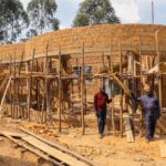 Two men inspect the wooden scaffolding of a brick building construction site outdoors.