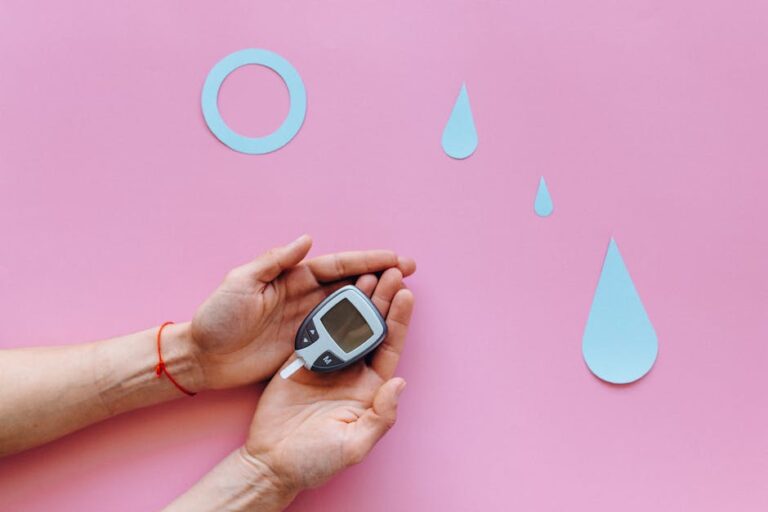 Hands holding a glucometer on a pink surface with blue diabetes symbols.