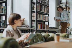 Young adults reading in a modern library with bookshelves, creating a cozy intellectual atmosphere.