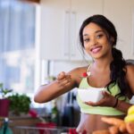 Smiling young woman in sportswear enjoying a healthy fruit snack indoors.