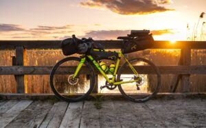 Bicycle loaded for travel resting against a wooden bridge at sunset.