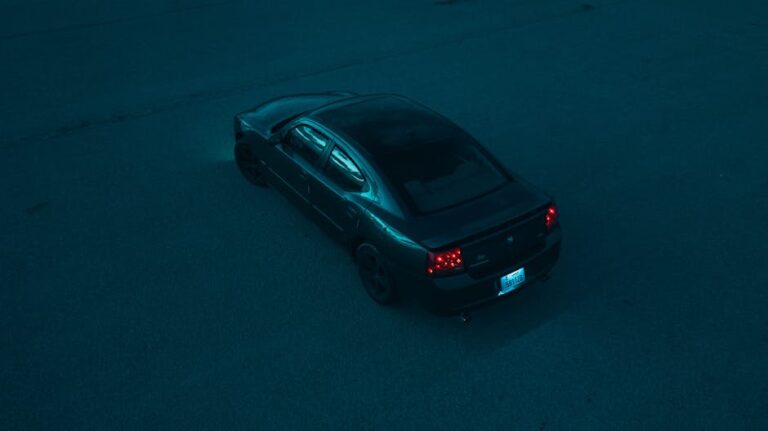 Aerial shot of a black Dodge car at night on an empty asphalt surface.