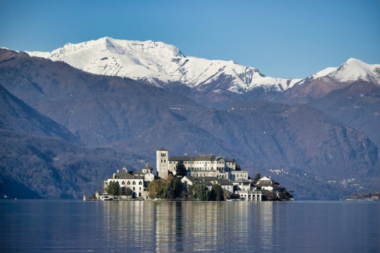 Stunning view of Isola San Giulio on Lake Orta with snowy mountain backdrop.