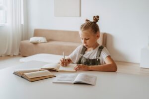 A young girl in a peaceful home setting focused on studying and writing in notebooks.
