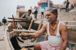 An elderly man paints a wooden boat on the ghats of Varanasi, showcasing traditional craftsmanship.