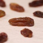 Detailed close-up image of dried raisins artfully arranged on a light wooden surface.