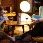 Couple enjoying a relaxed evening playing a board game with wine in a cozy home setting.