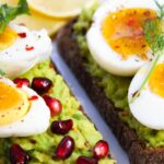 Savor this delicious avocado toast topped with soft-boiled eggs and garnished with pomegranate seeds.