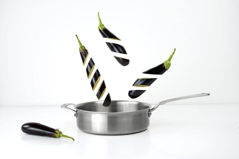 Creative image of sliced eggplants floating above a stainless steel pan against a white background.