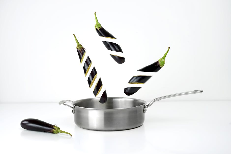 Creative image of sliced eggplants floating above a stainless steel pan against a white background.