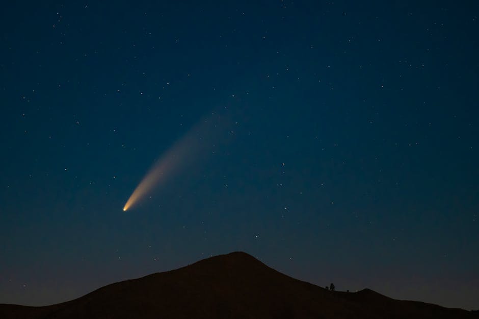 A breathtaking capture of a comet streaking across a star-filled night sky above a mountain silhouette.