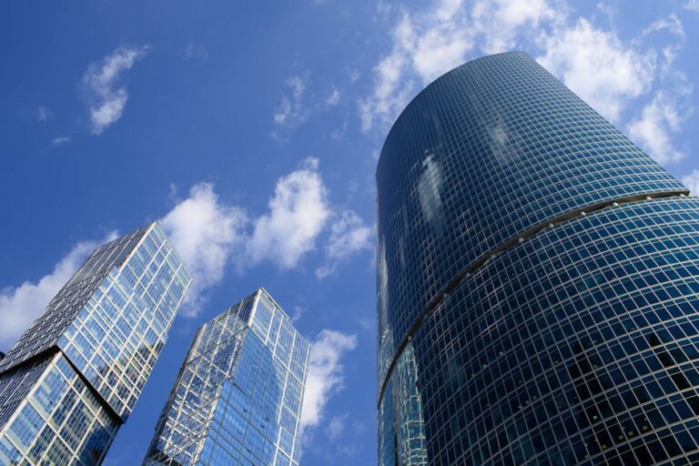 High-rise glass buildings reaching towards a bright blue sky, symbolizing modern architecture.