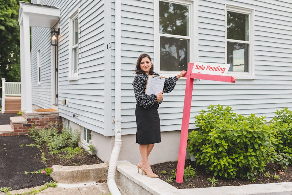 Real estate agent standing by a home with a sale pending sign, holding documents.