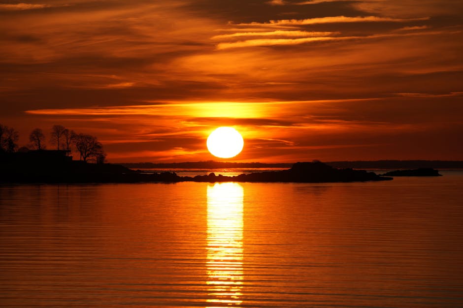 Vibrant sunset over ocean, reflecting vivid orange hues across calm waters.