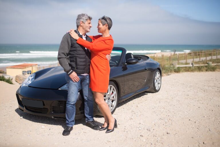 Elderly couple enjoying a moment together by a black cabriolet at a scenic beachside location.